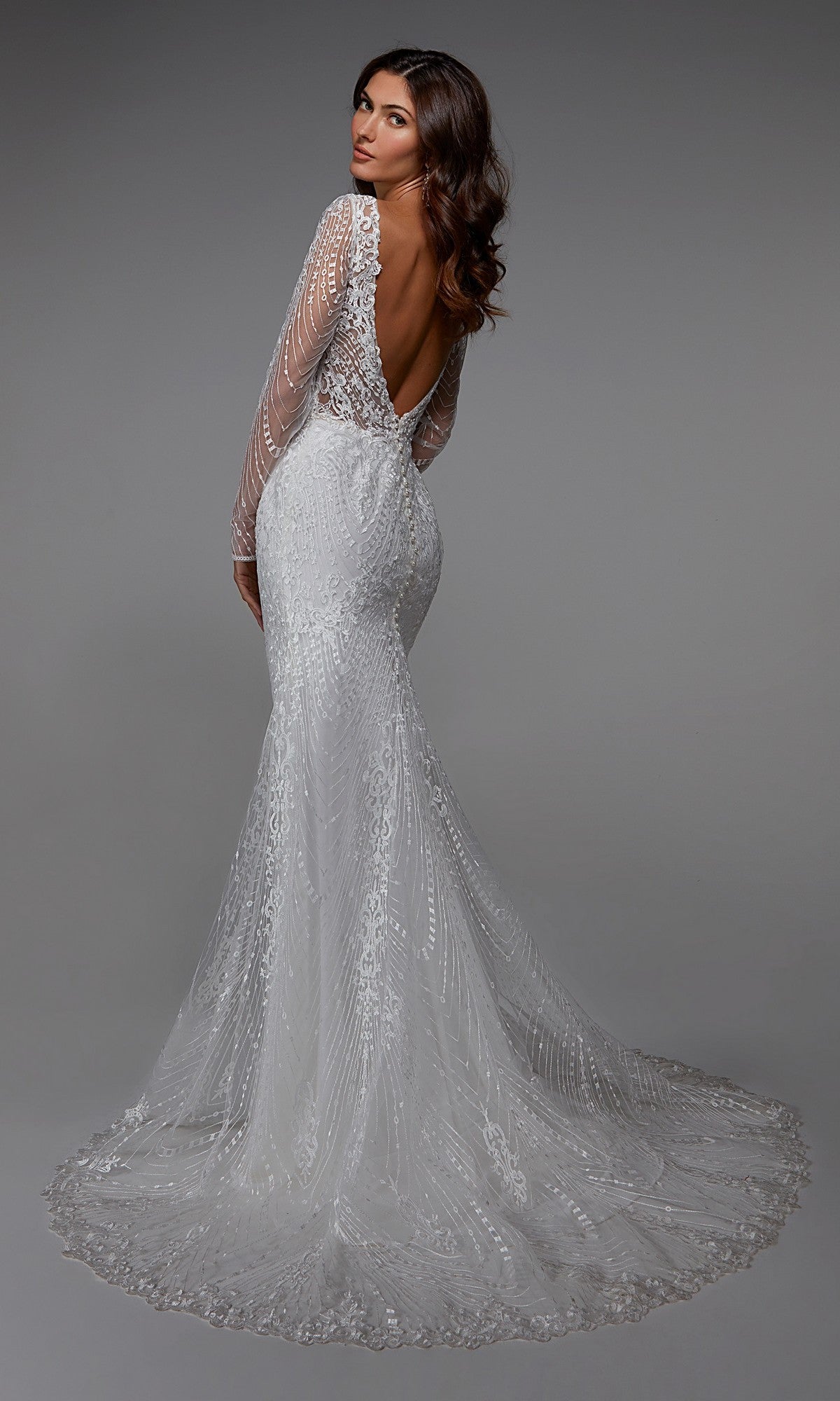 A woman in the Alyce 7030 long formal dress—a fitted, long-sleeved, backless white lace gown with a flowing train—stands against a plain gray background.